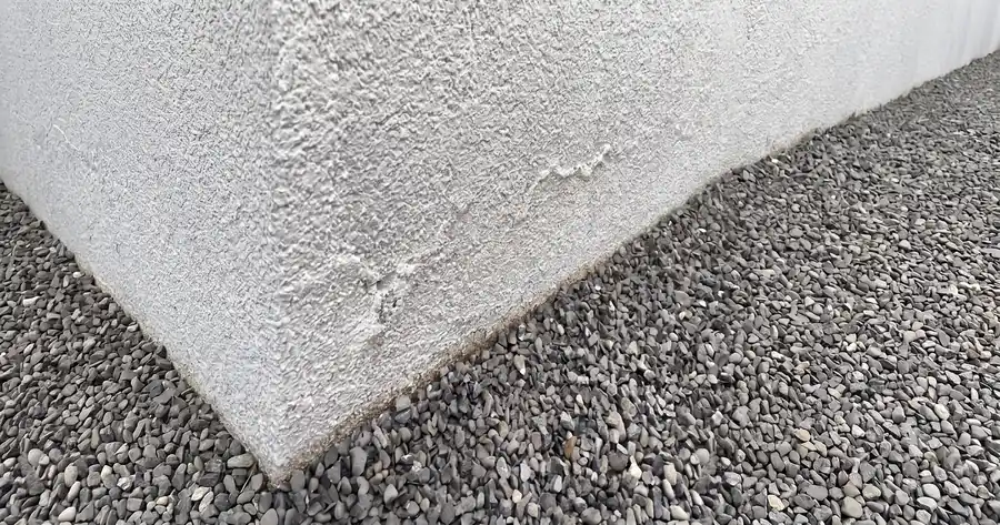 Estuco de muro perimetral en contacto directo con el suelo natural, con manchas de humedad visibles en el paramento